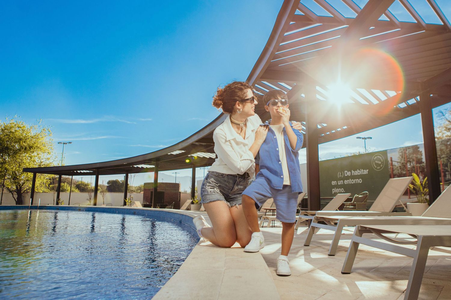 Couple relaxing by luxury pool with modern pergola and bright sunlight.