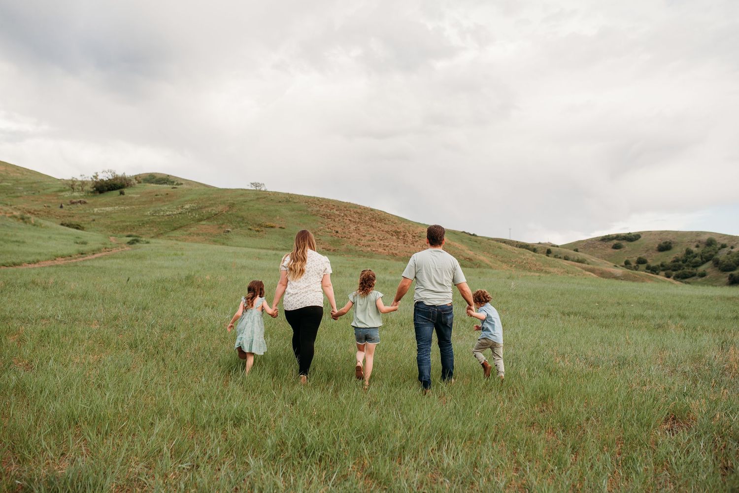 Family walking hand in hand through green rolling hills during sunset photo session.