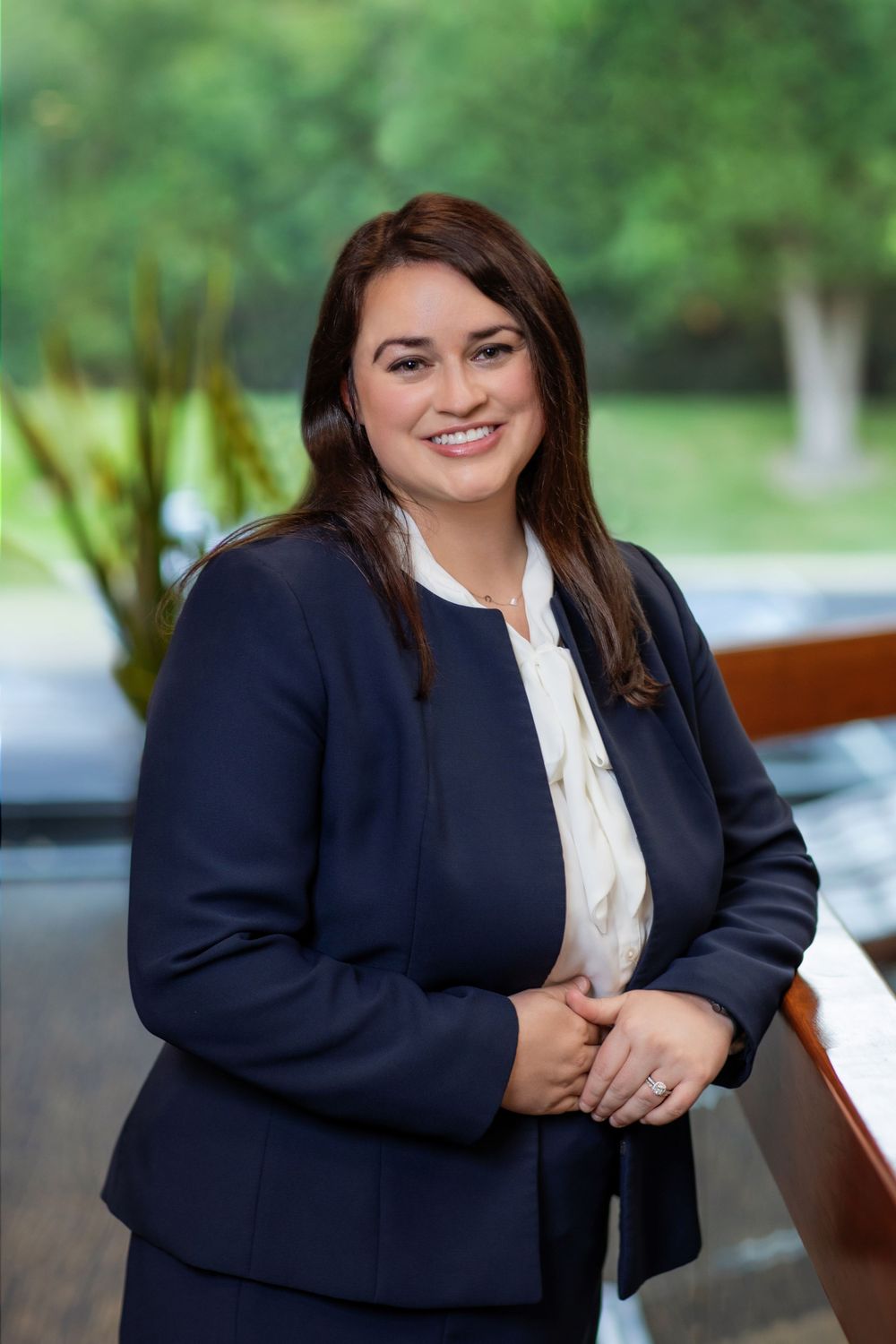 Professional portrait of a woman in a navy blazer and white blouse against a blurred outdoor background.