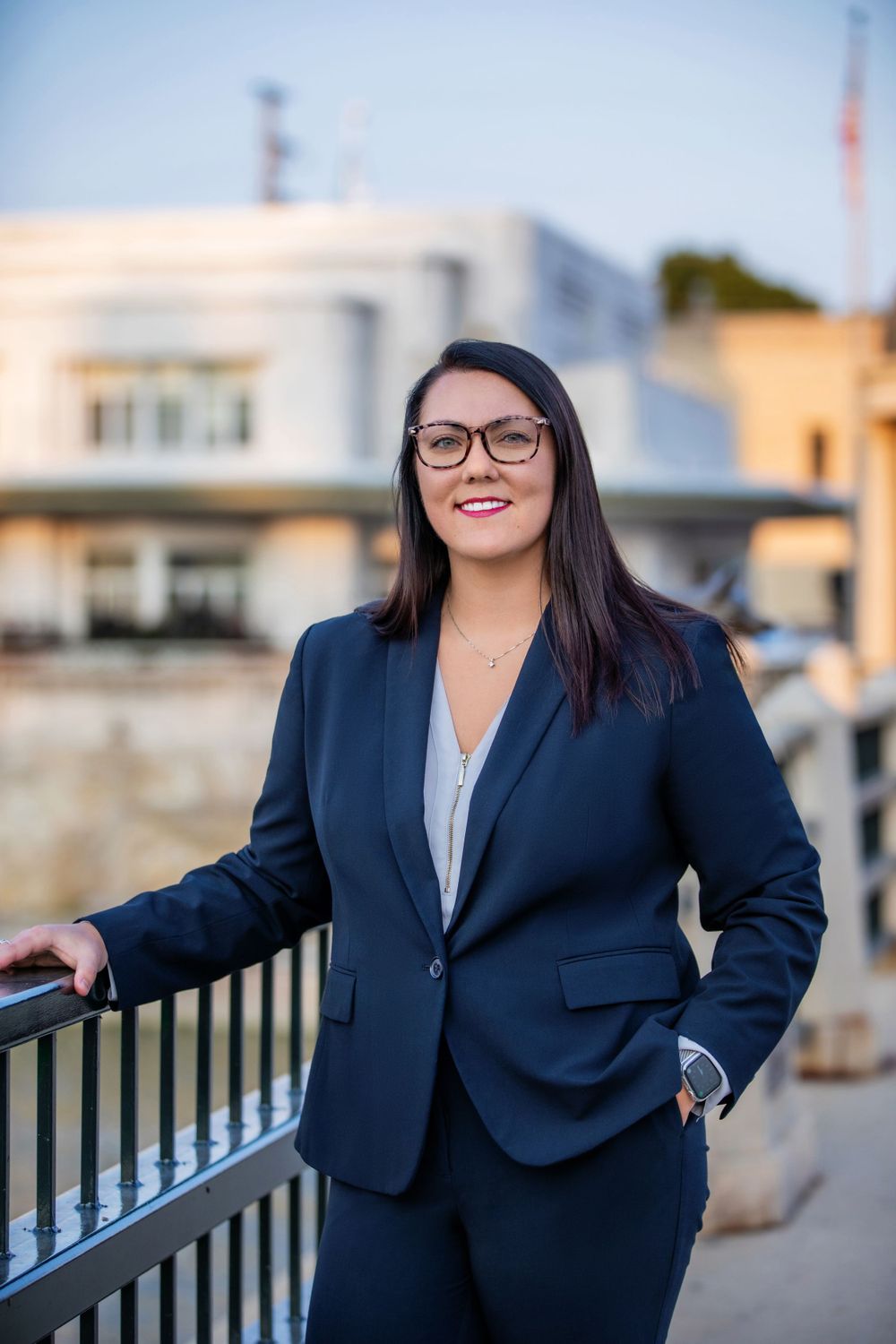 Professional attorney in dark suit and glasses leaning on outdoor railing during golden hour.