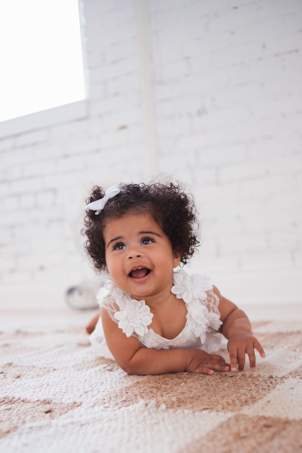 Baby in white lace romper crawling on carpet with joyful expression.
