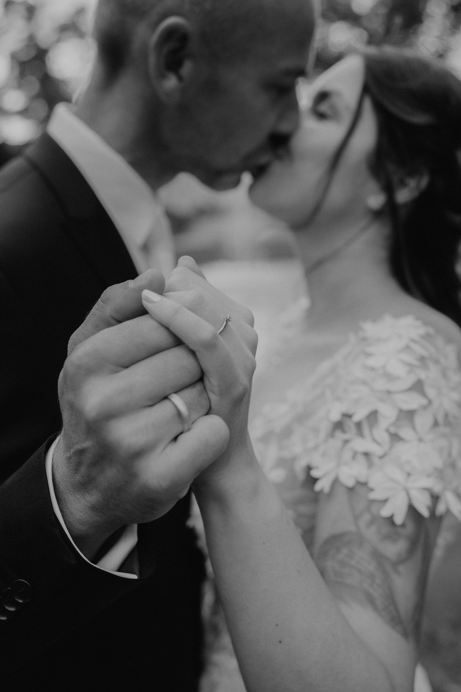 Close-up black and white photo of newlyweds sharing an intimate moment showing wedding rings.