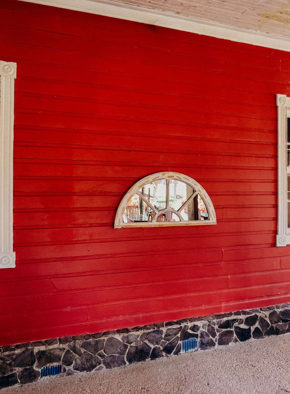 Red wooden barn wall with arched mirror window and stone foundation base.