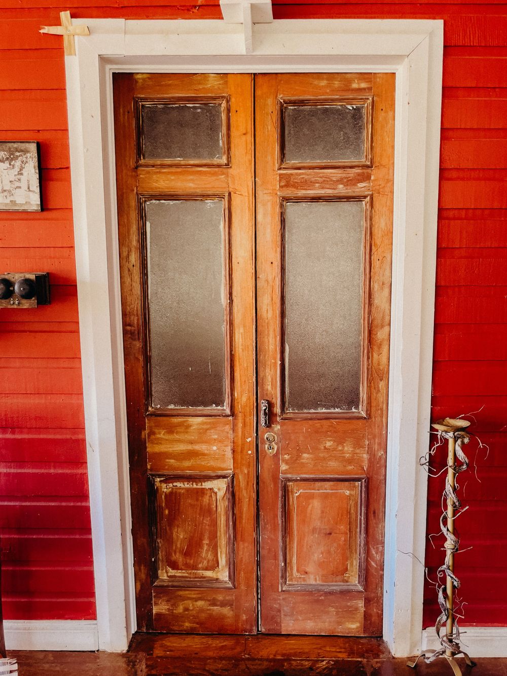 Vintage wooden double doors with frosted glass panels set in white trim against a red wooden wall interior.