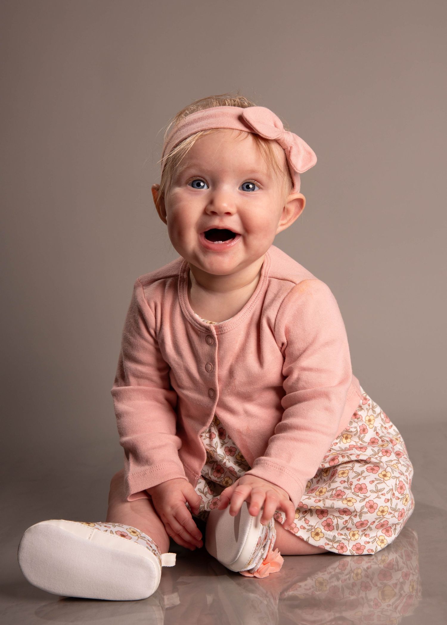 Baby in pink sweater and floral dress smiles and plays on neutral gray studio backdrop in progressive sequence.