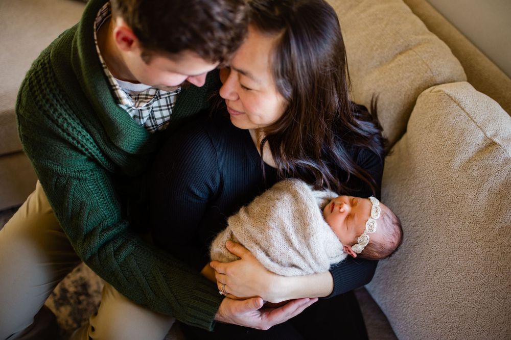 Mom and dad holding their newborn girl in their home in Madison WI and snuggling in close to each other