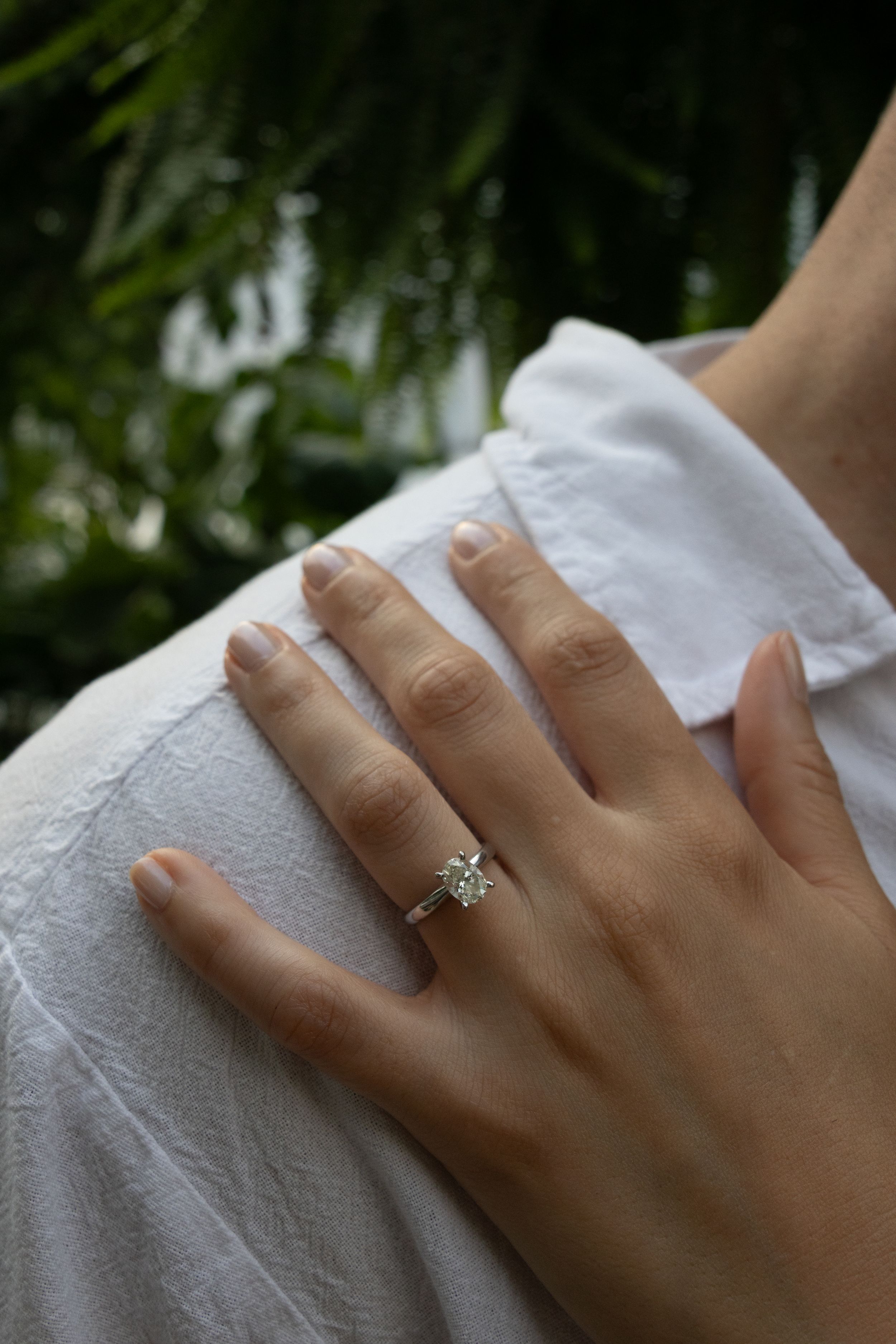 Close-up of an engagement ring on a hand resting against white fabric.