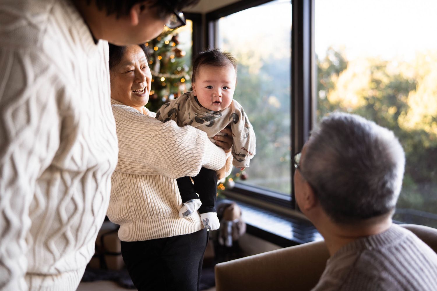 Family members gather near a sunlit window and Christmas tree on a cozy afternoon sharing a tender moment together.