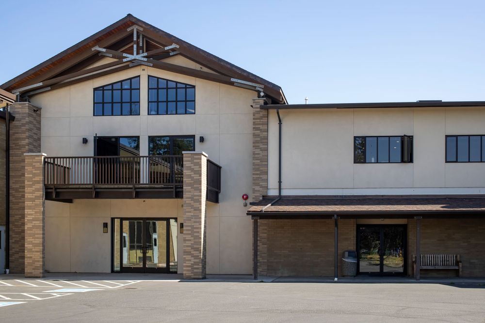 Modern two-story building entrance with balcony and large windows beneath an angled roof design.