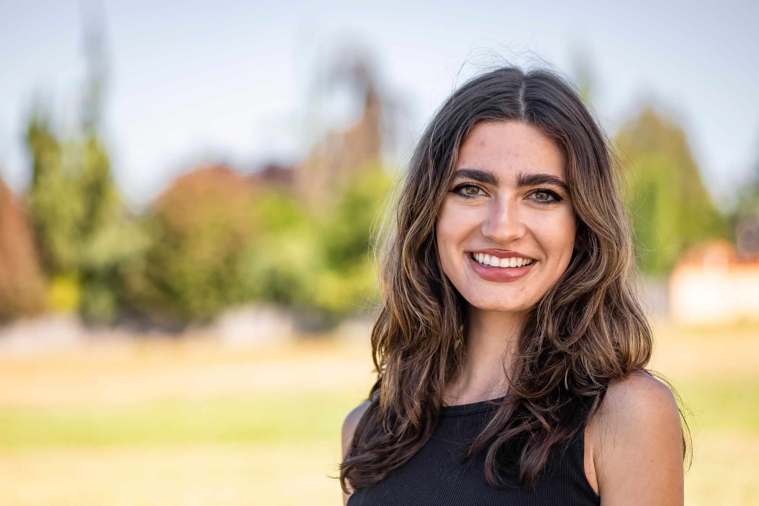 A casual portrait of a smiling person outdoors with trees in the background.