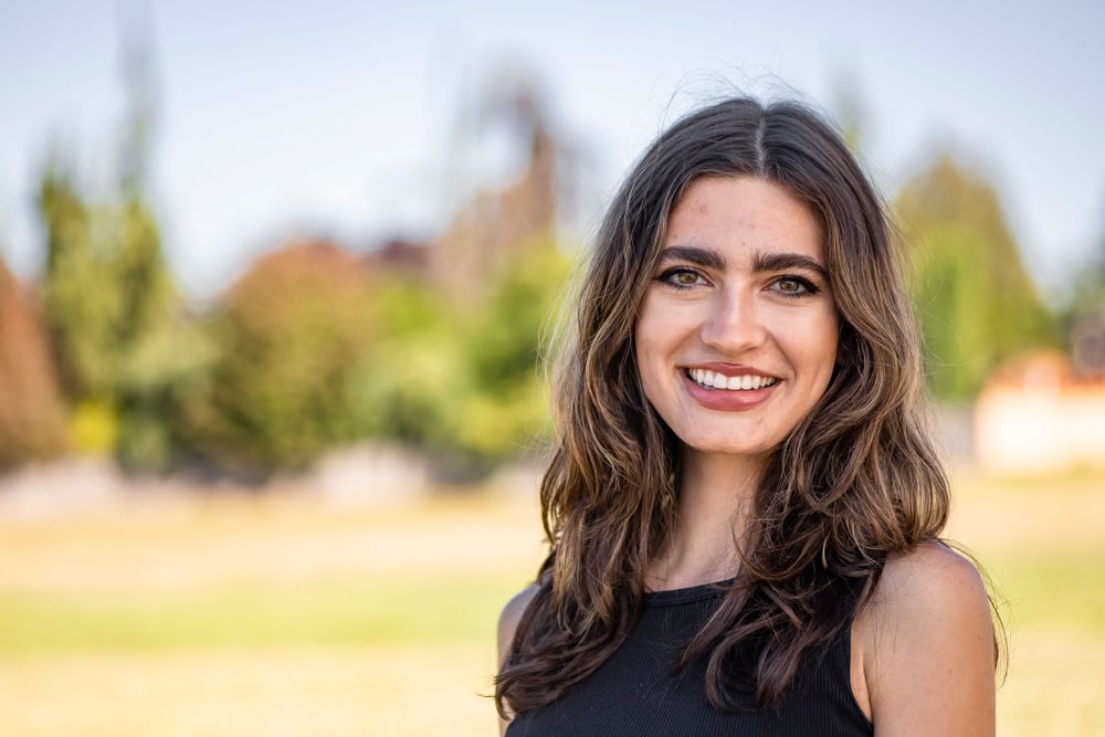 A casual portrait of a smiling person outdoors with trees in the background.
