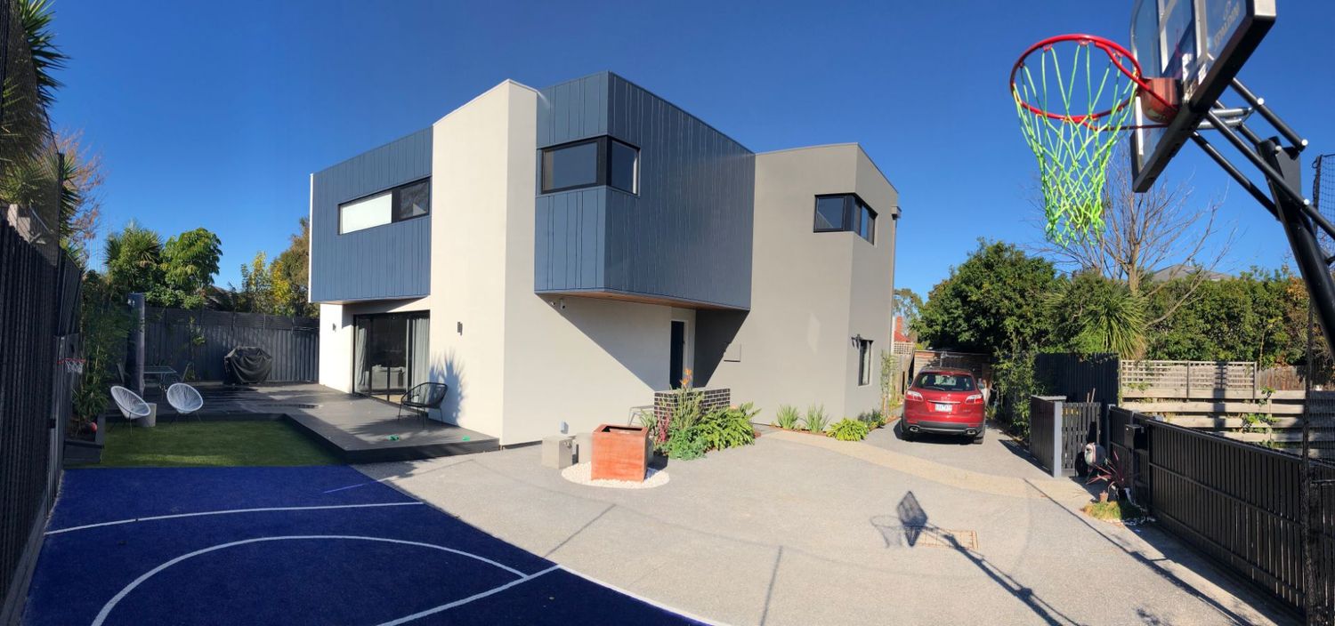 Modern home exterior with basketball court featuring colorful hoop and grey contemporary architecture.