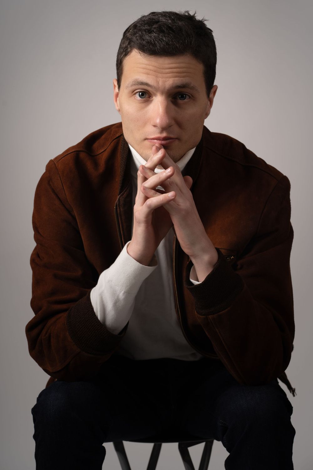 Portrait series showing contemplative poses in brown jacket against grey backdrop.