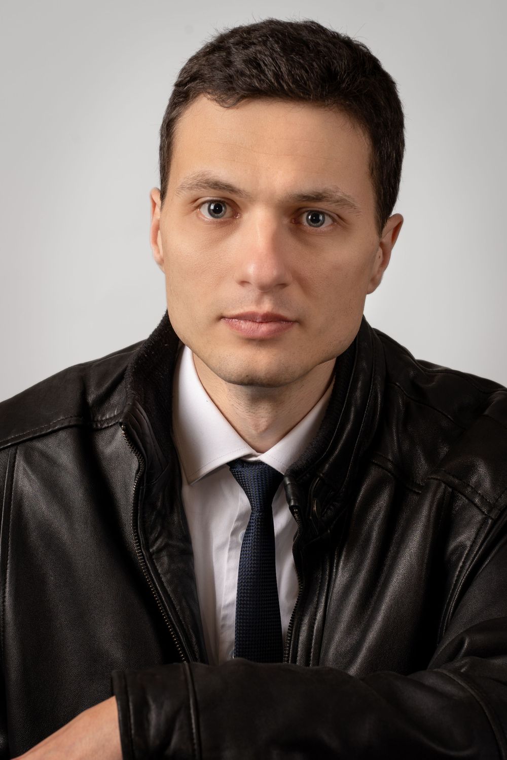 Professional headshots of person in black leather jacket against grey background.