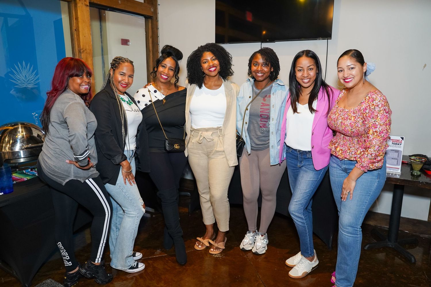A diverse group of friends pose together smiling at a casual indoor gathering.