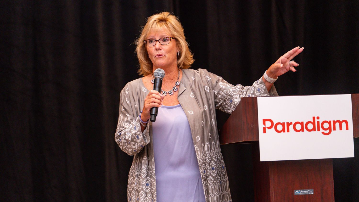 Speaker presenting on stage with Paradigm banner in background.