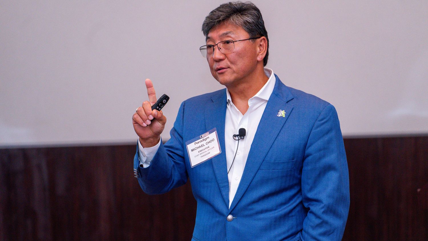 Professional speaker gestures during business presentation wearing navy suit.
