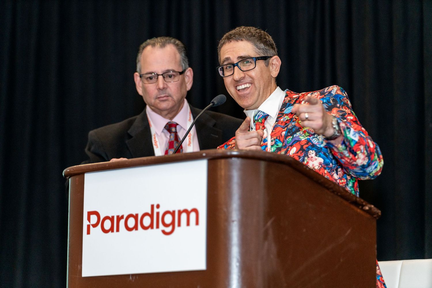 Presenters stand at a podium with a Paradigm sign during what appears to be a conference or business presentation.