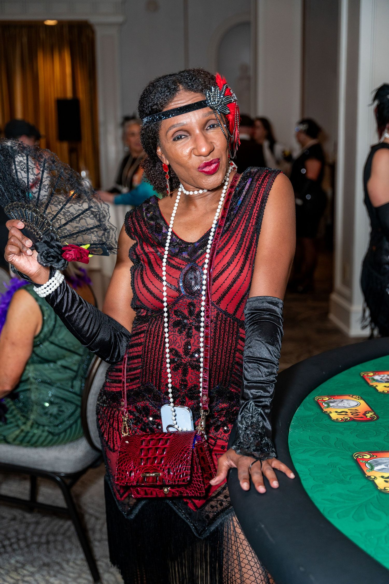 Casino party attendee in a burgundy and black dress shows enthusiasm while playing at a green felt gaming table.