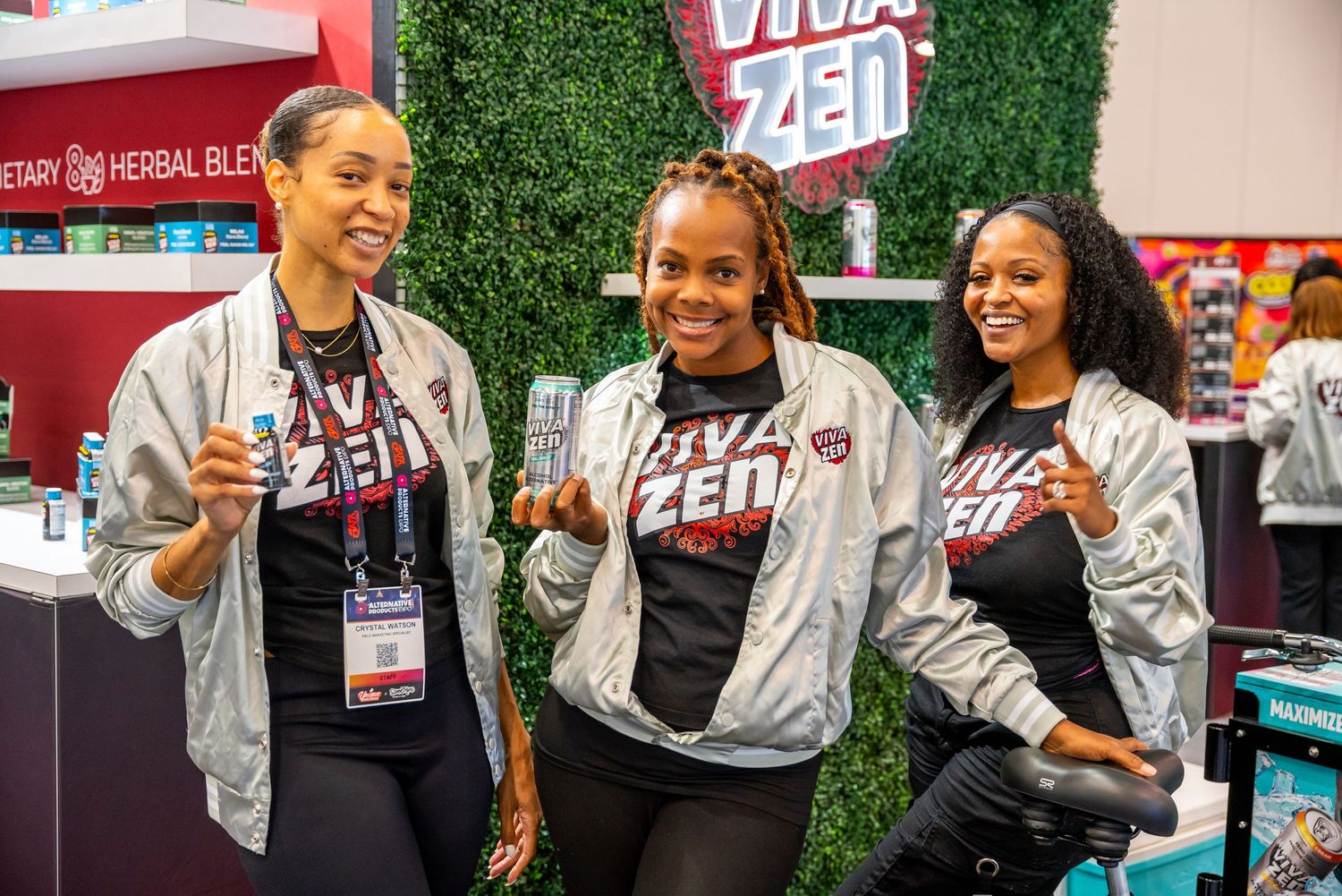 Three people in matching athletic wear pose with beverages at promotional event.