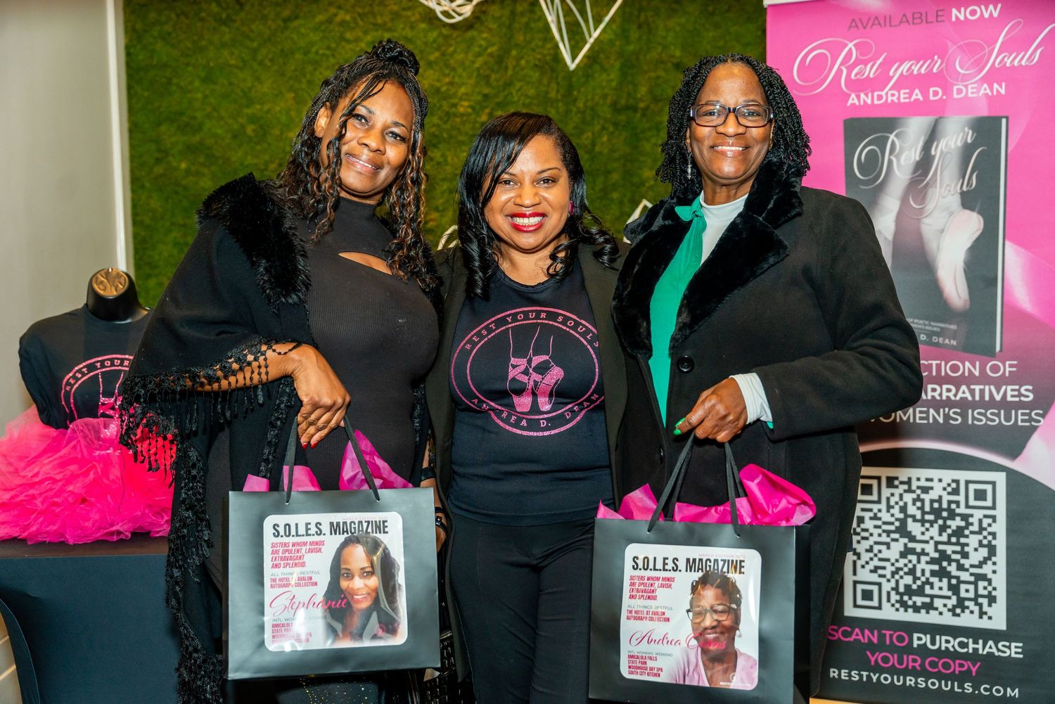 Three people at a professional networking event with merchandise display and pink highlights in the backdrop and decor.