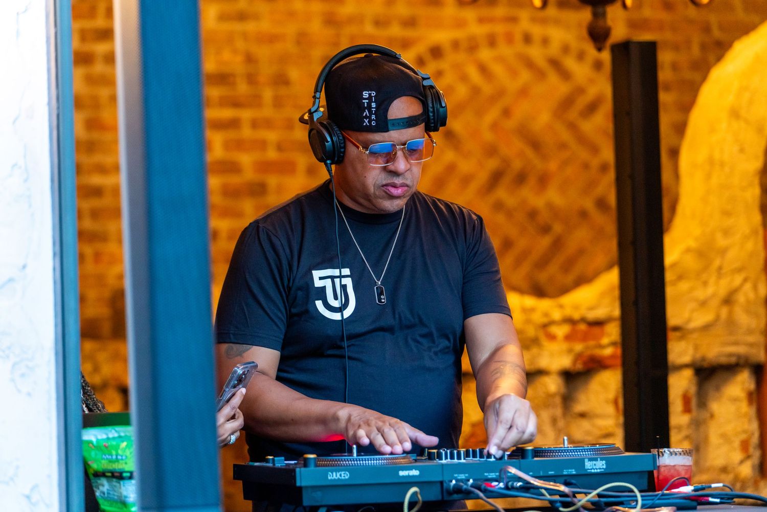 DJ performs with equipment at nighttime event with brick wall backdrop.