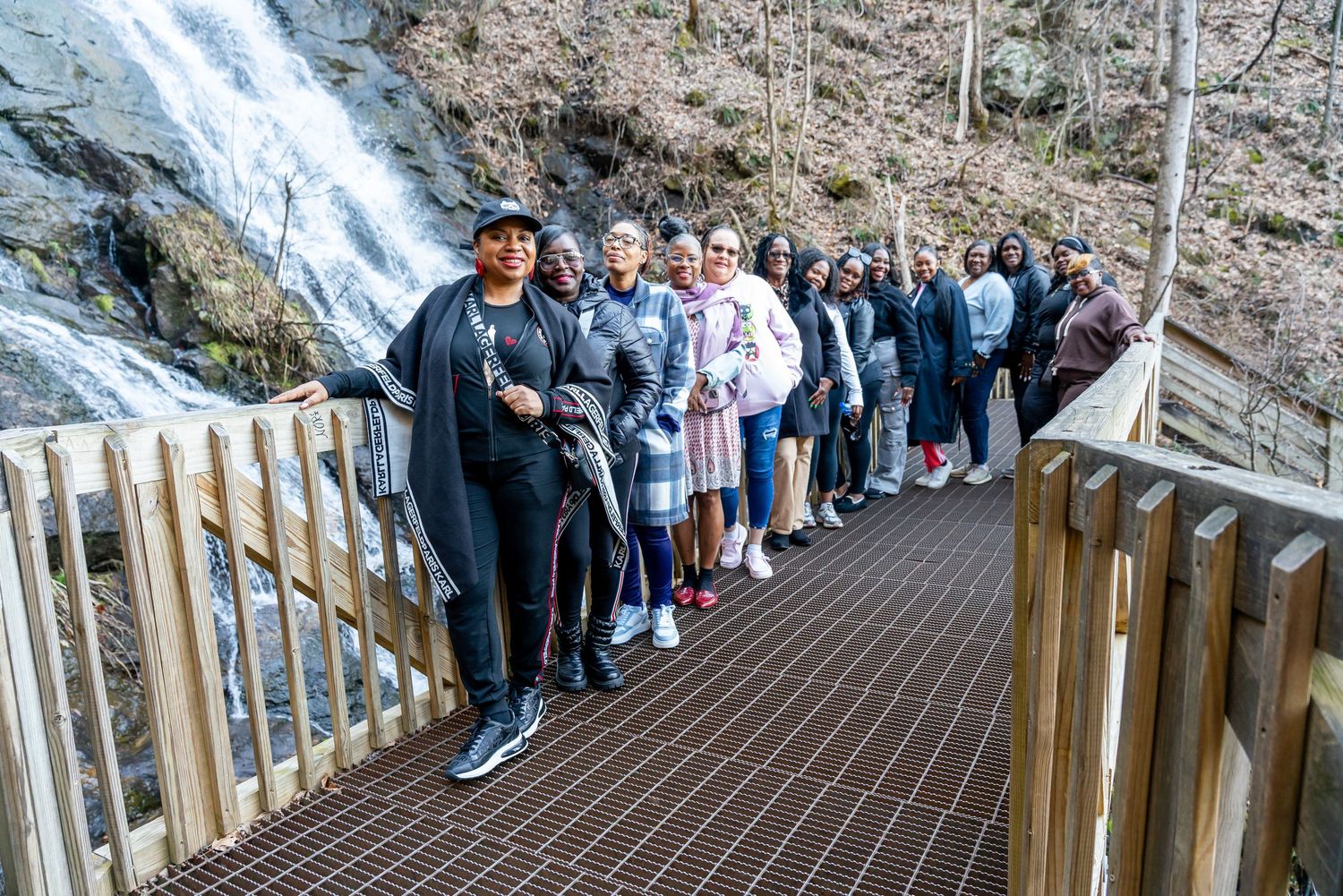 A line of visitors standing on a wooden boardwalk viewing platform next to a cascading waterfall.