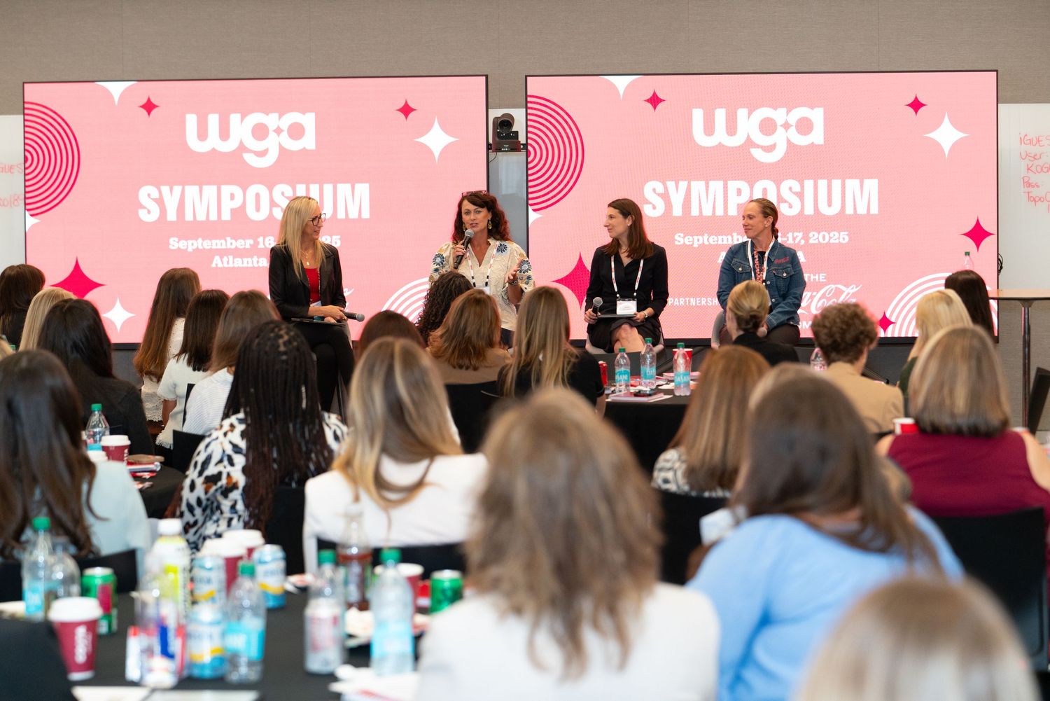 Group of people seated at a long table attending a pink-themed workshop or presentation event.