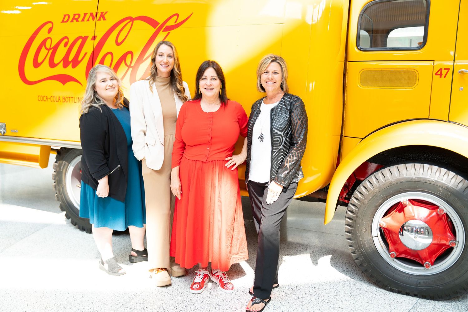 A bright yellow Coca-Cola delivery truck is parked outdoors with people standing nearby.