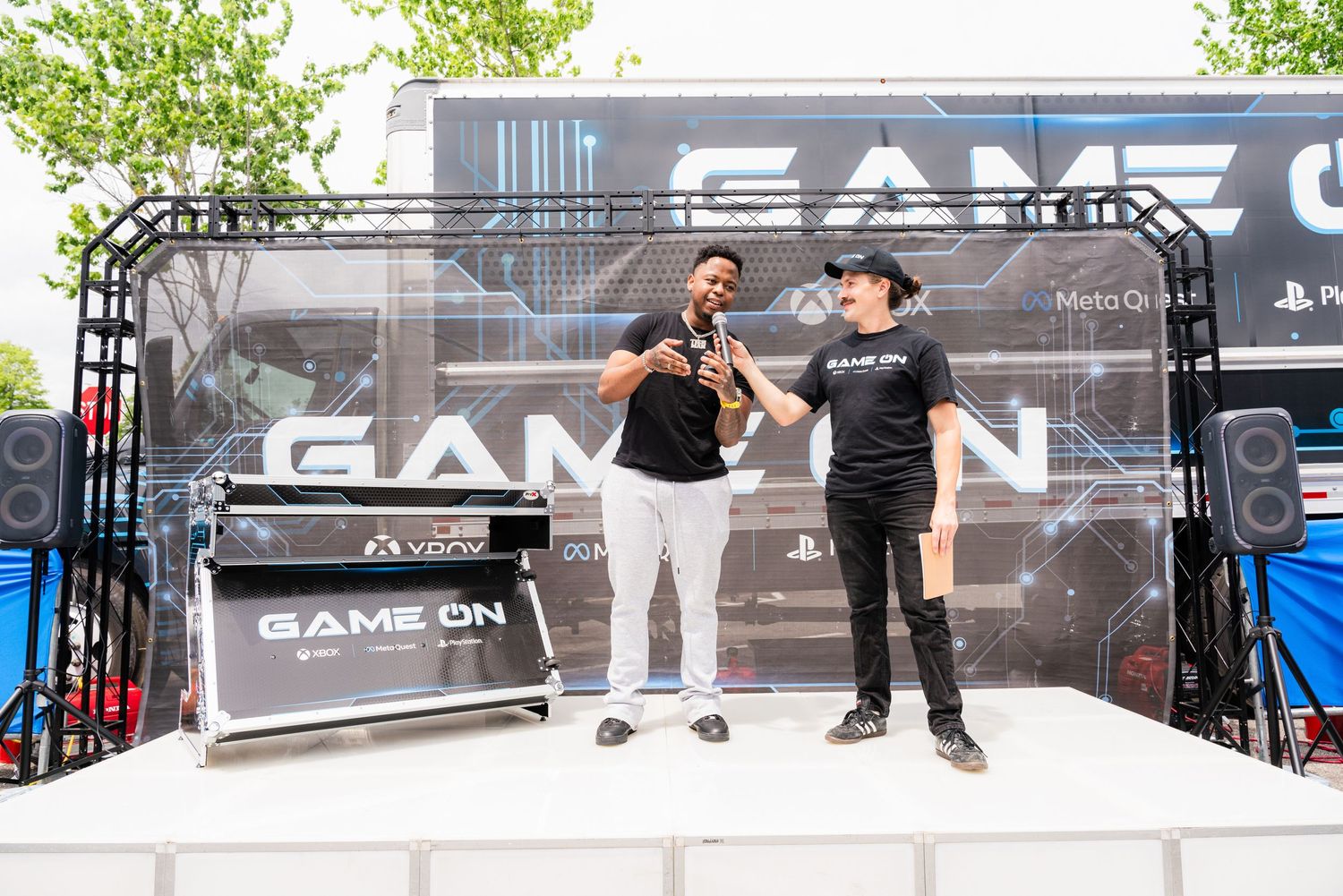 Two performers entertain crowd on outdoor stage with GameOn backdrop.