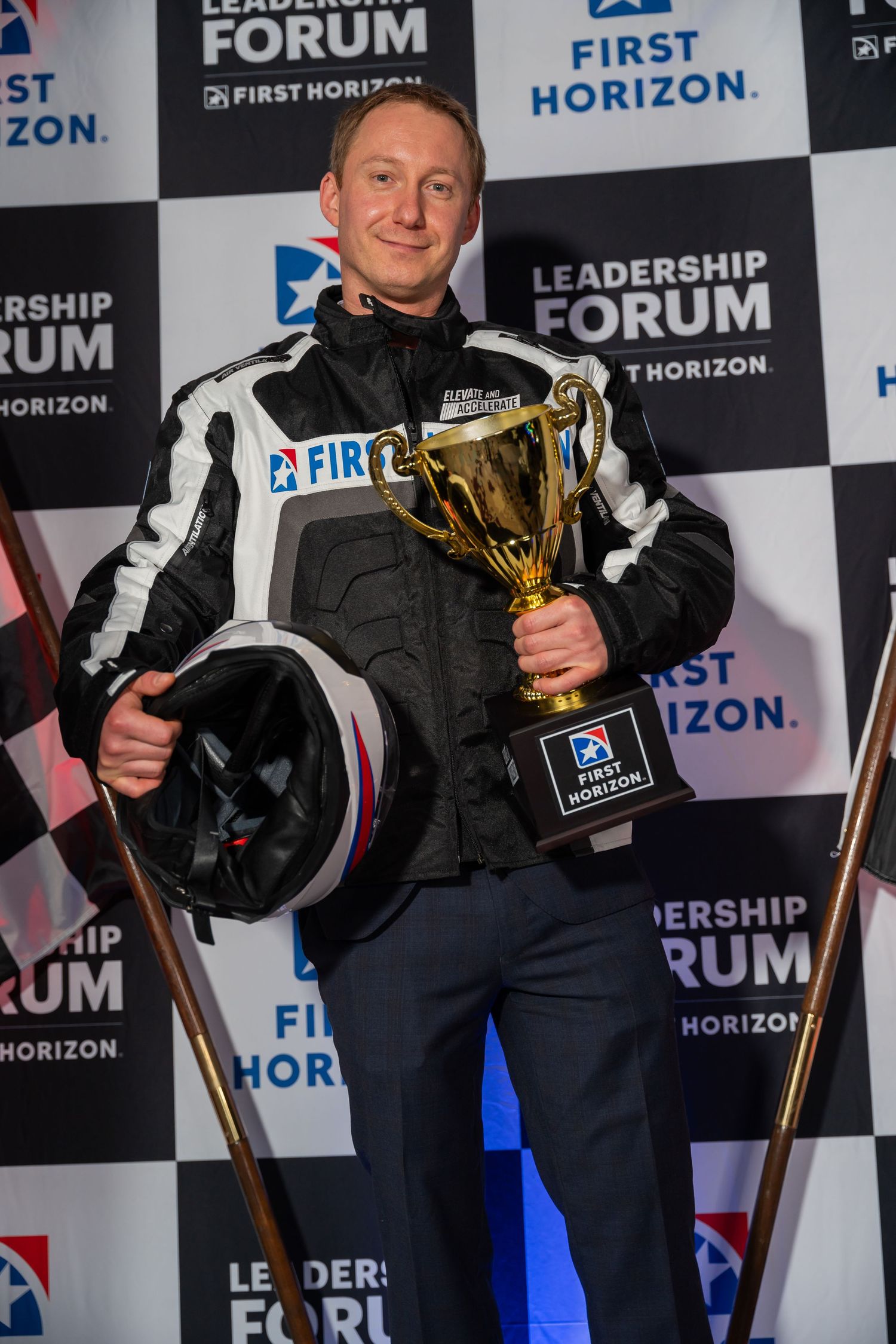 Racing champion holds trophy and helmet at First Horizon leadership forum event.