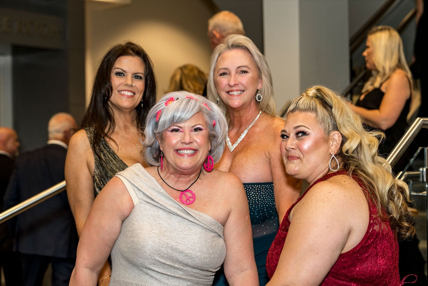 A small group of women in formal attire pose together at an elegant indoor event.