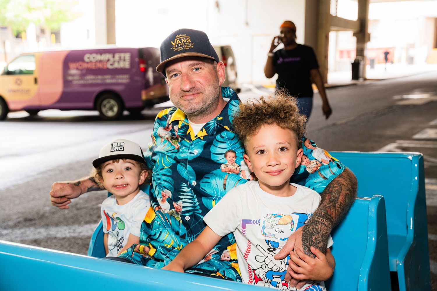 Family wearing matching Hawaiian shirts enjoying a ride in blue cart.