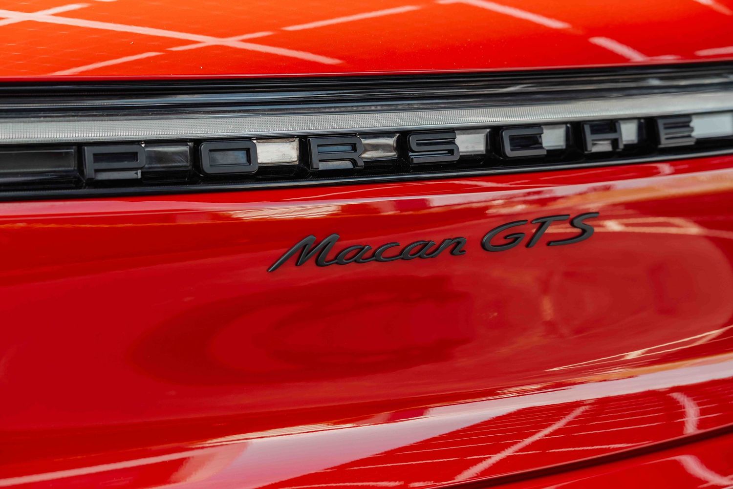 Close-up detail of Macan GTS badge on red Porsche vehicle.