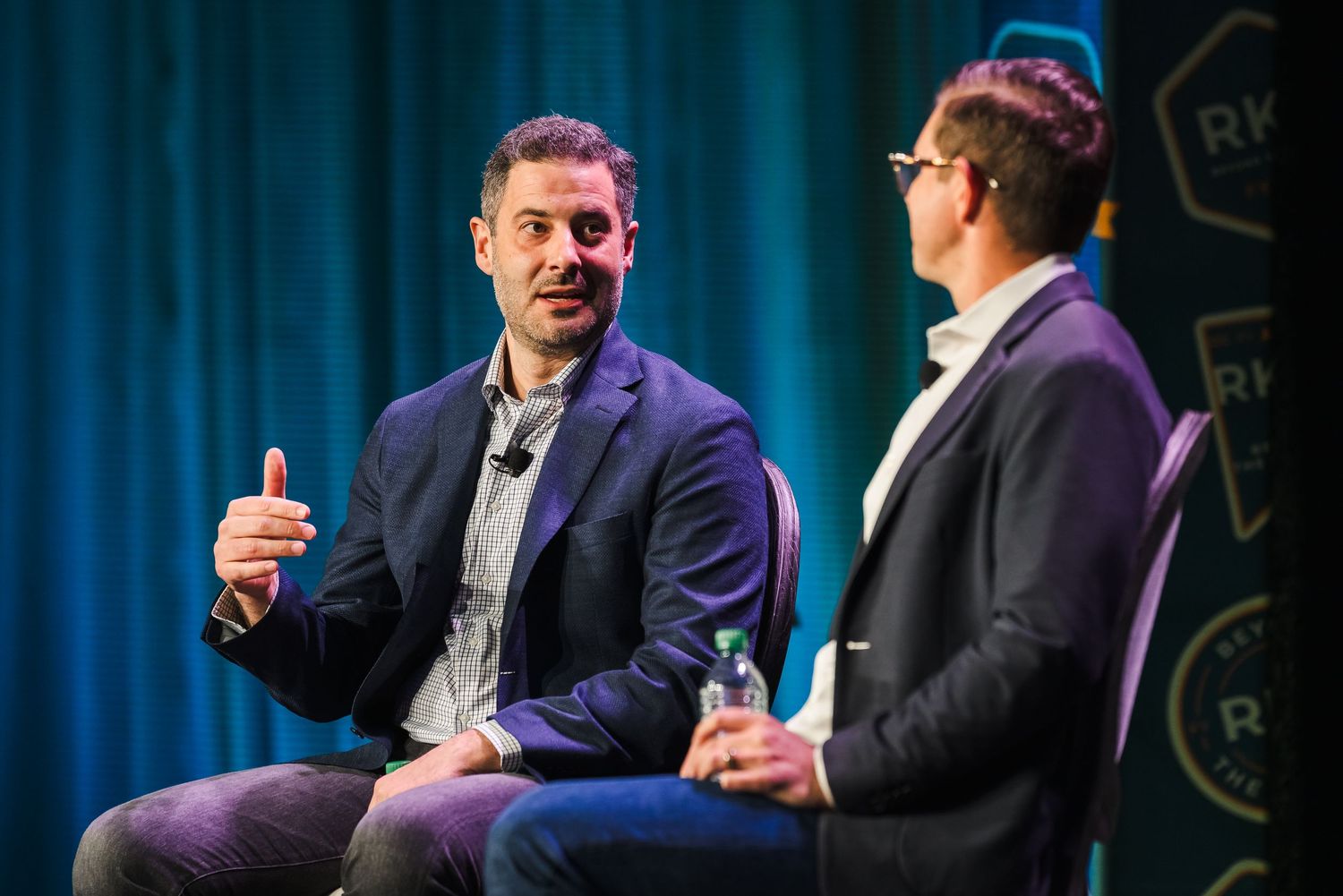 Two people in business attire having an animated conversation on stage at a professional event.