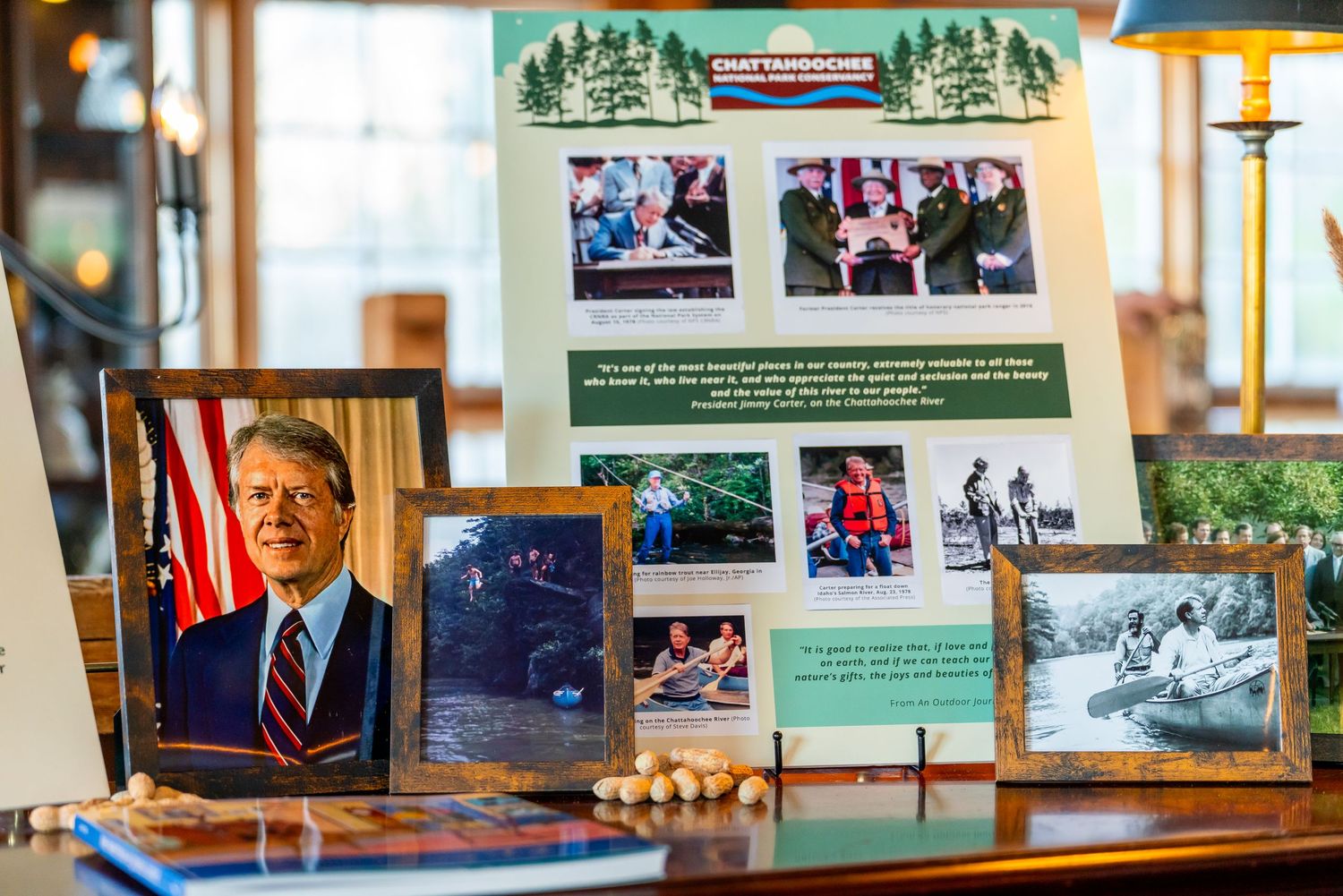 A framed photo and presentation display board with multiple images sits on a wooden table with a lamp nearby.
