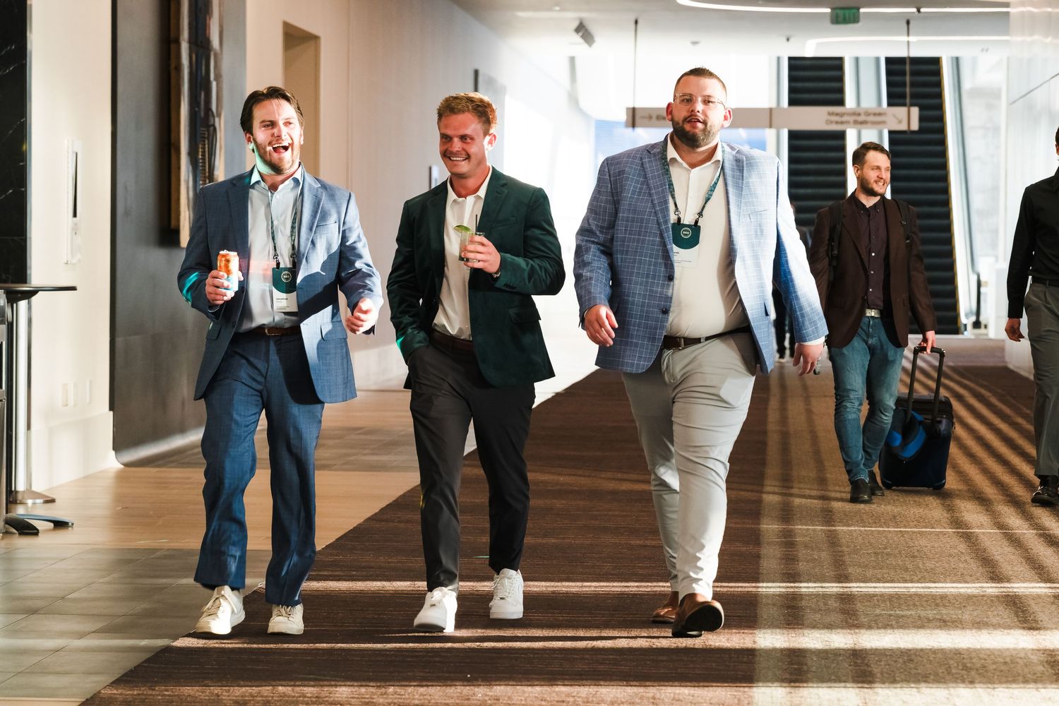 Business professionals walk together through a bright office hallway with sunlight streaming through windows.
