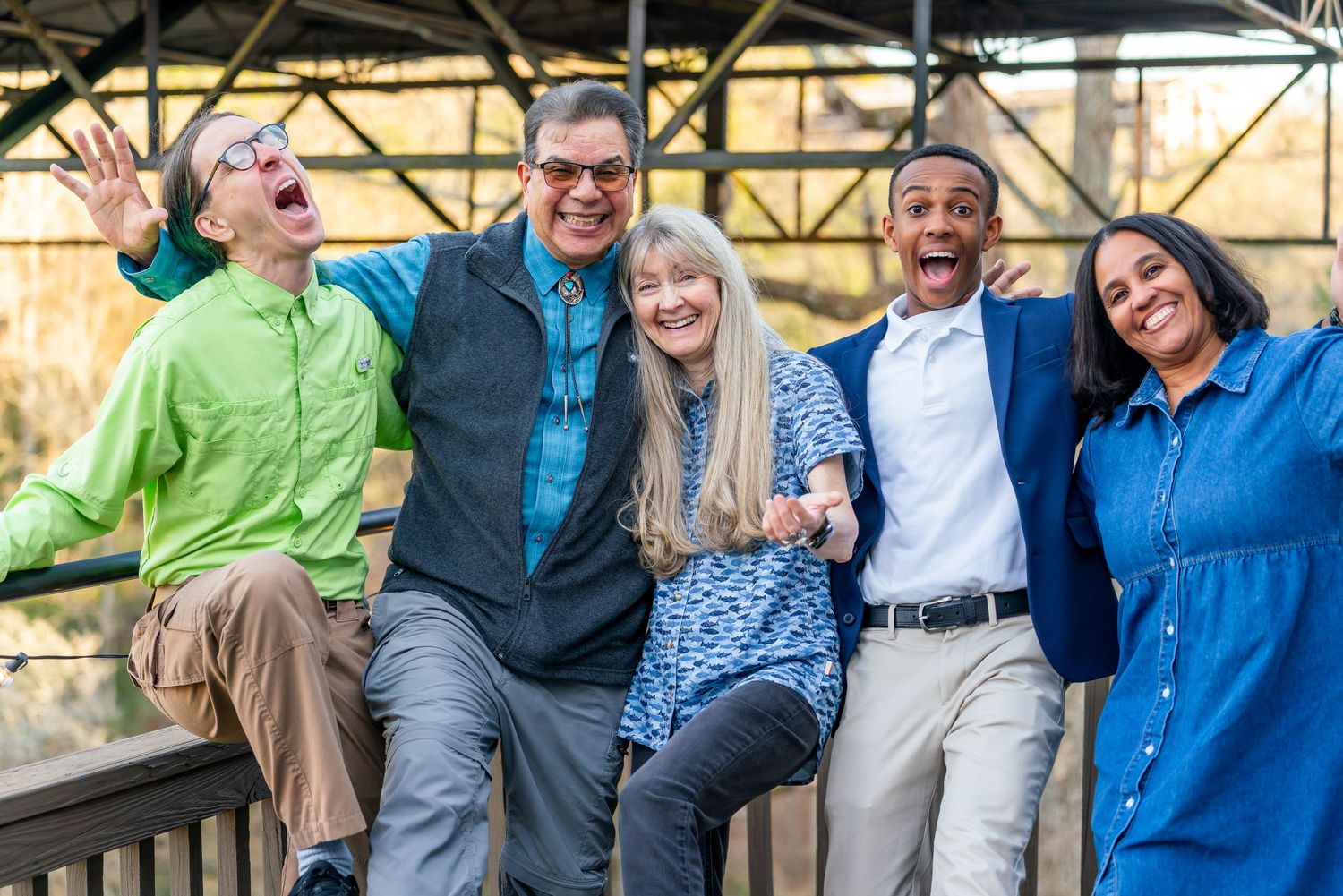A diverse group of people sitting together on a bench outdoors, laughing and having fun in casual clothing.