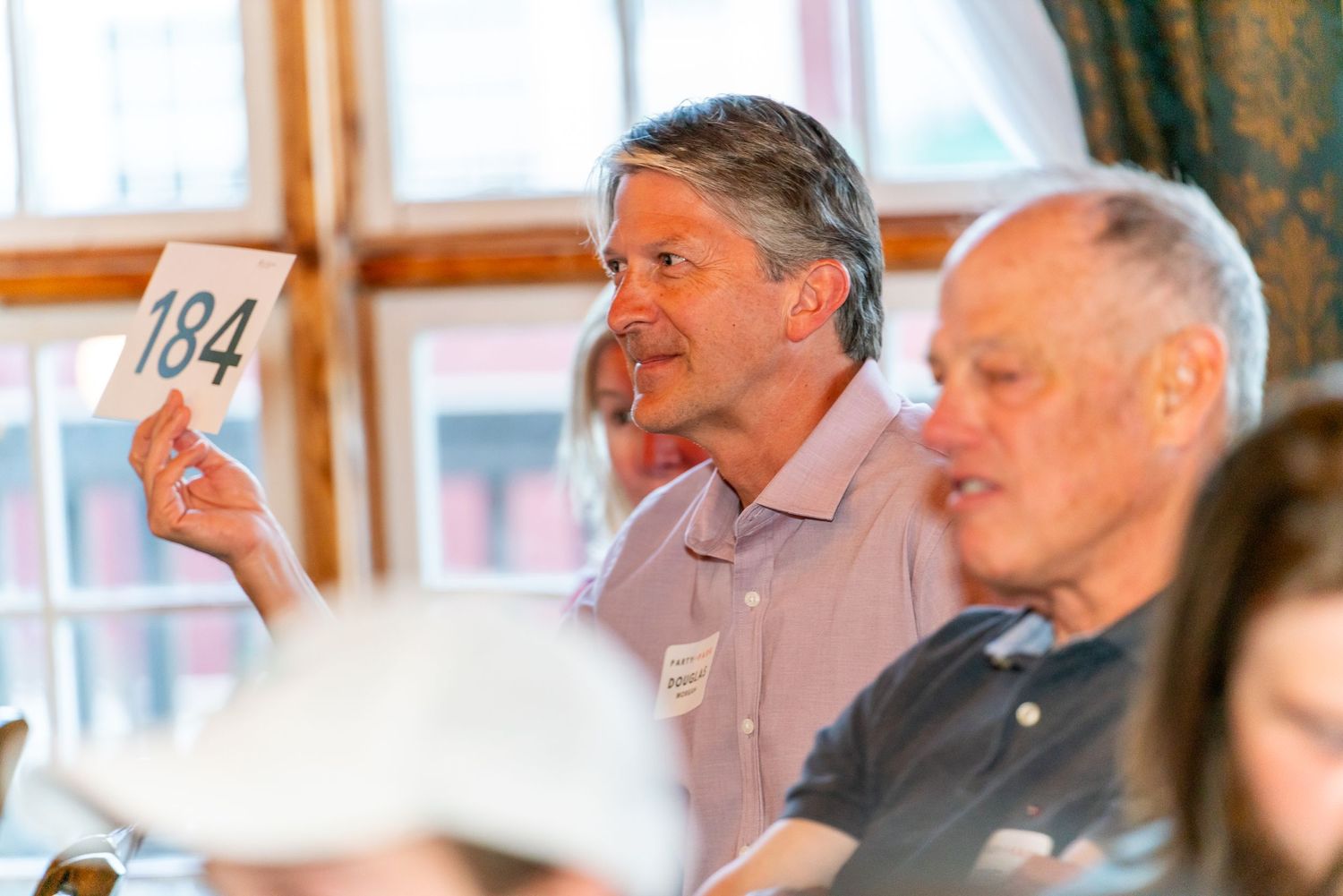 Attendees at an auction hold up number cards to bid on items during a live sale event.