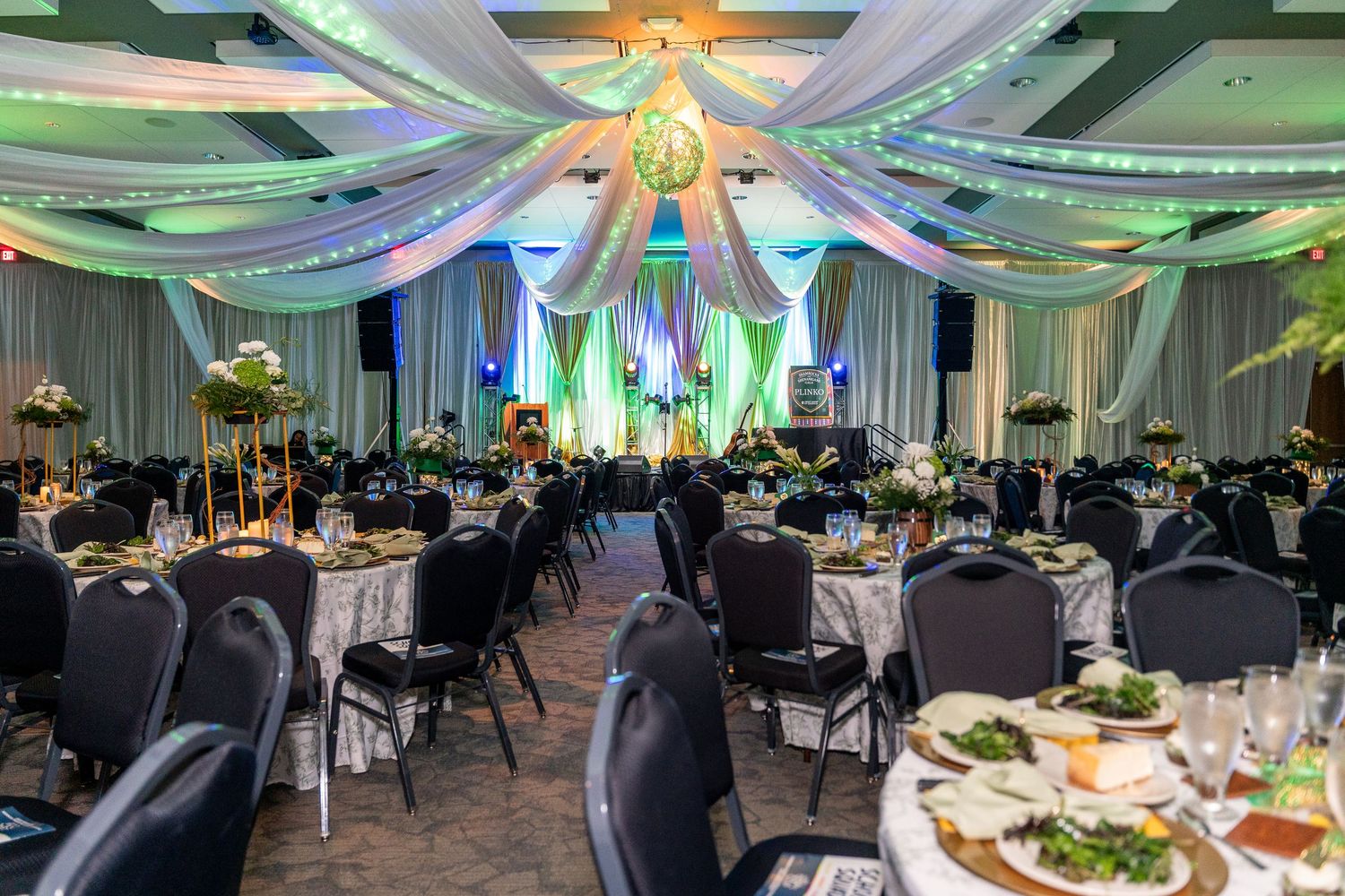 Elegant banquet hall decorated with teal and white fabric draping from ceiling with round tables set for formal dinner event.