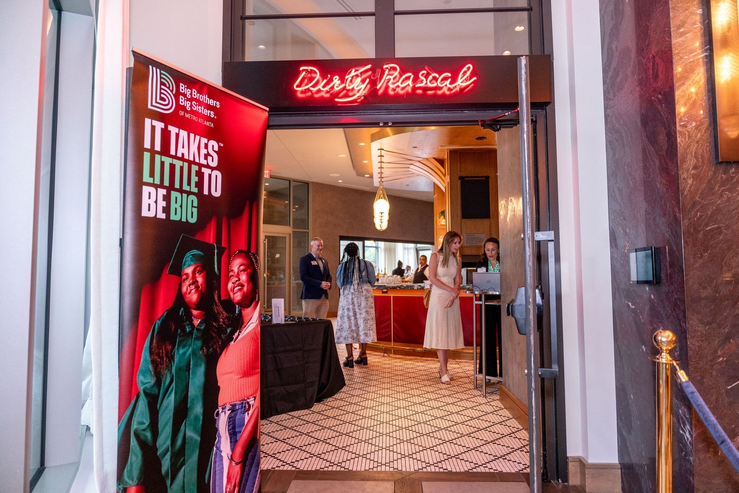 Red neon signs illuminate a dimly lit hallway with mirrored walls and patterned floor tiles inside a commercial building.