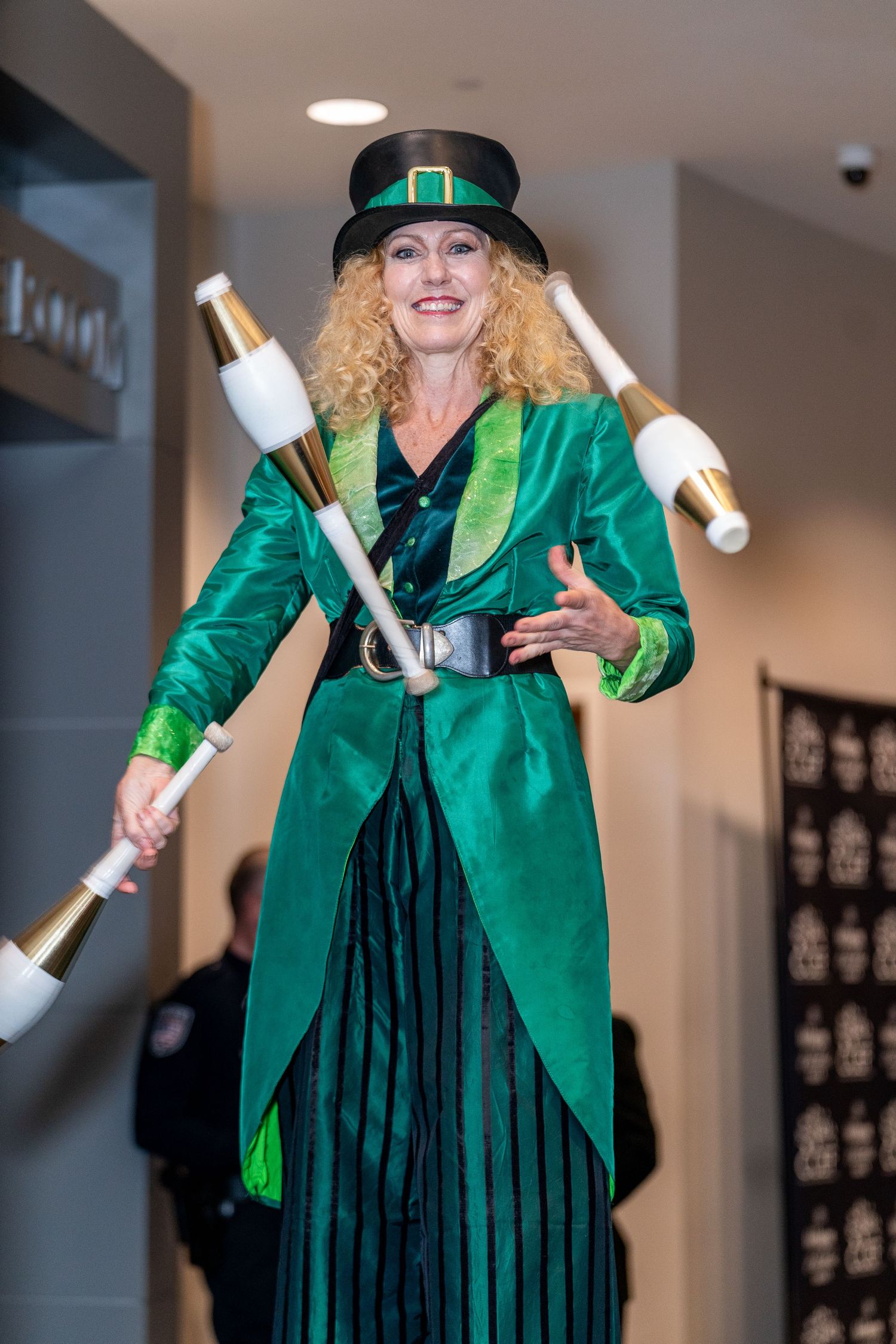 Performer in emerald green coat and top hat juggles white pins while wearing festive St. Patrick's Day themed attire.