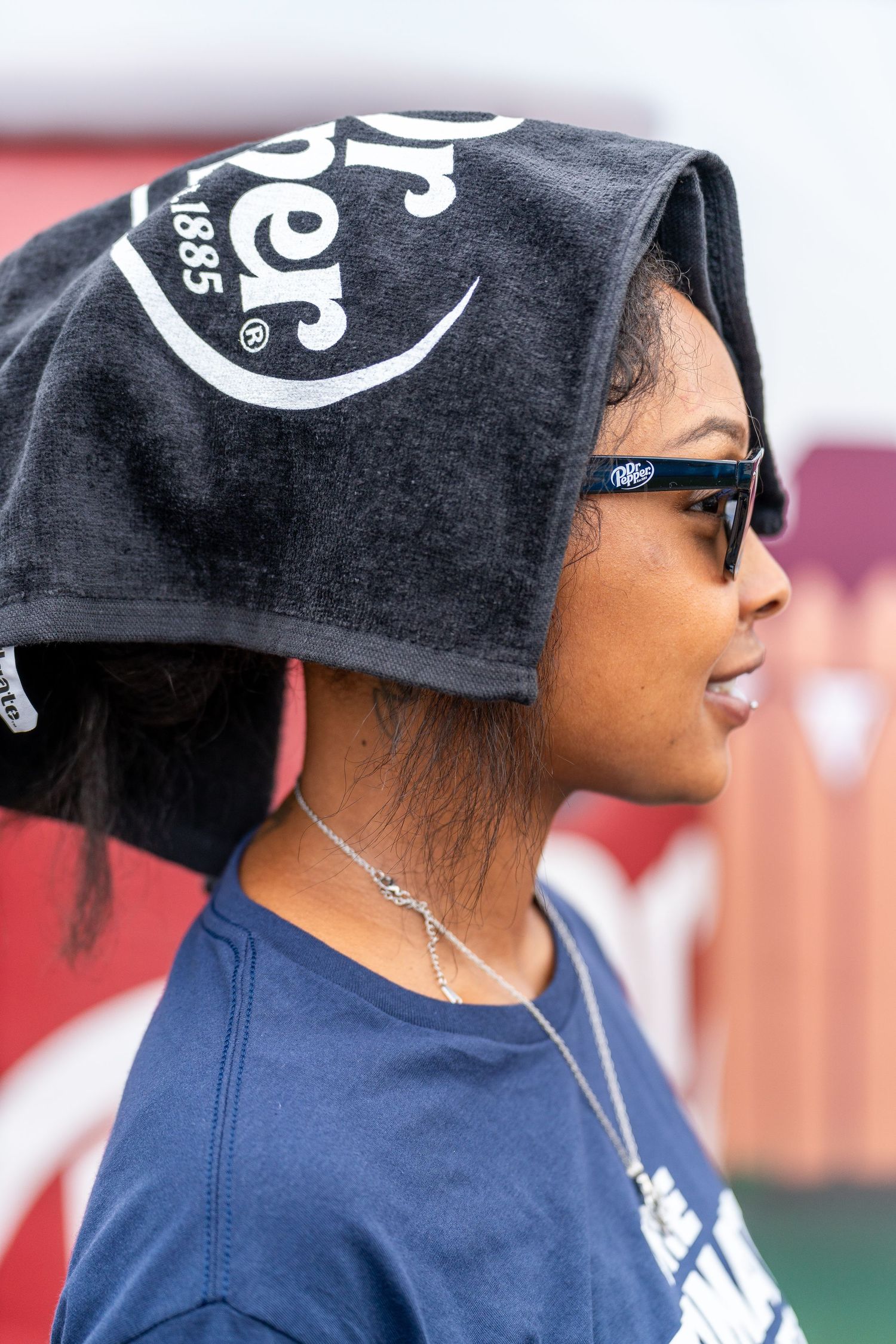 A person wearing sunglasses and a black baseball cap with white lettering looks to the side in a blue shirt.