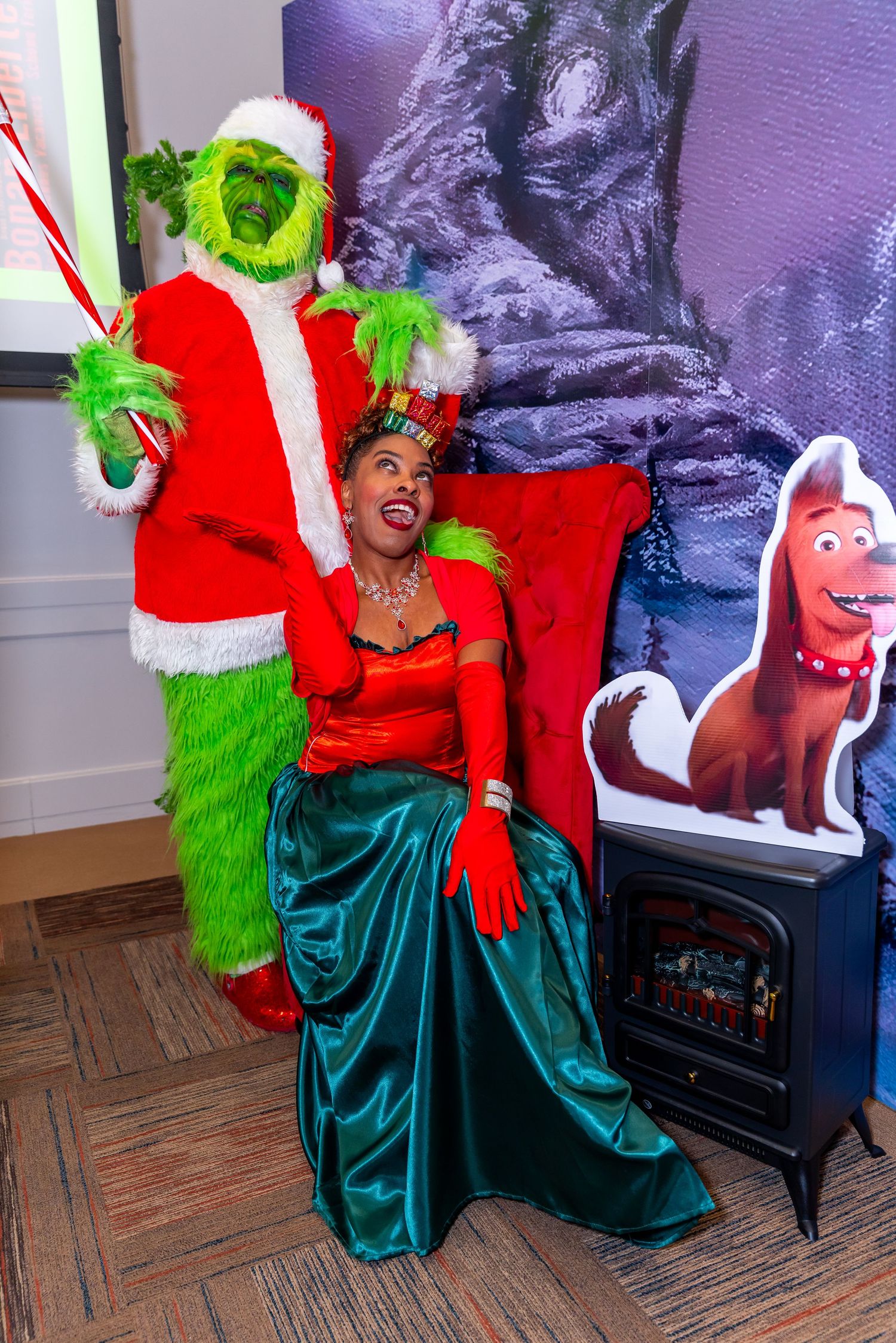 A festive holiday scene with the Grinch costume and someone in a red and green outfit posing next to cartoon dog decorations.