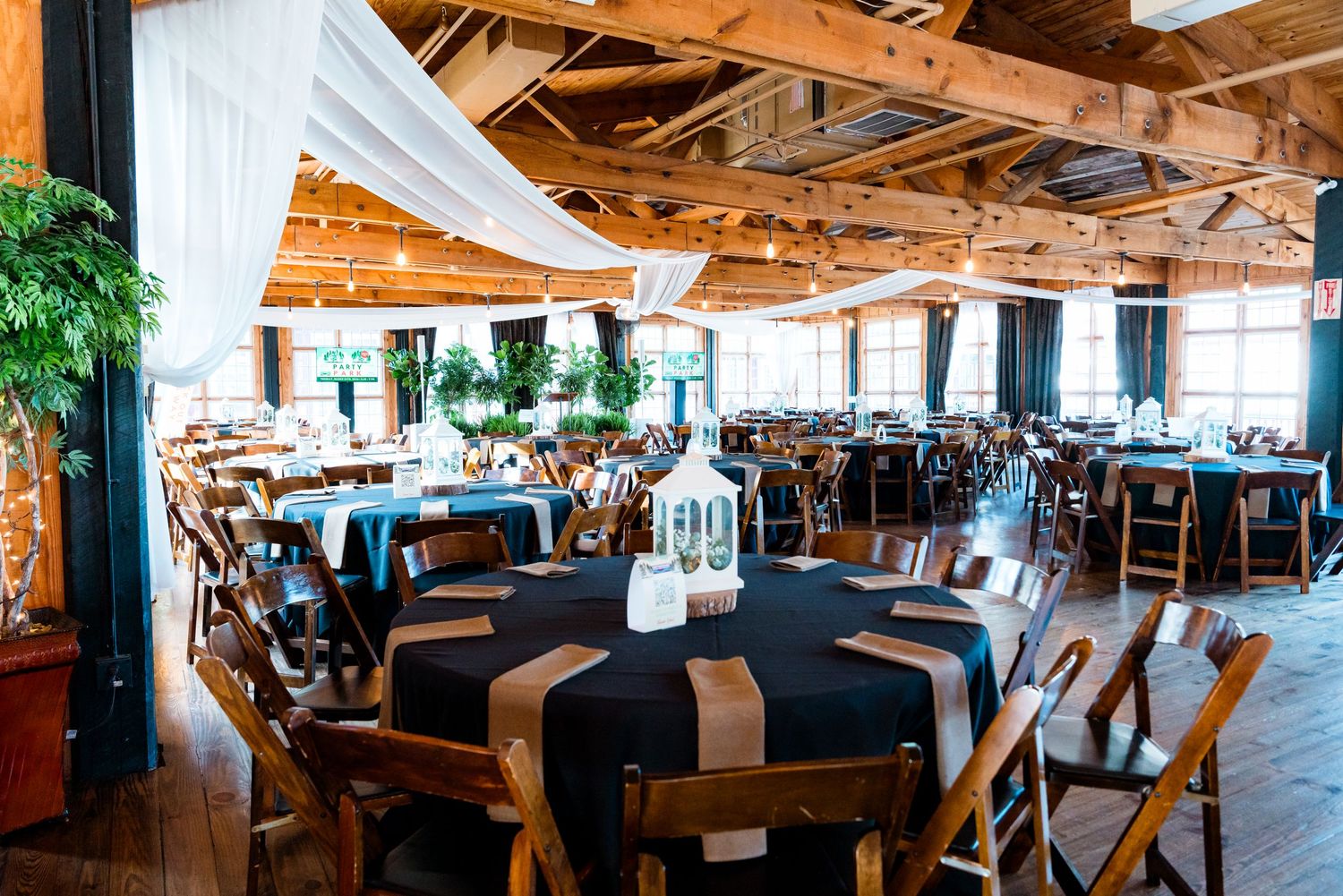 Rustic wedding reception venue with round tables, black linens, wood chairs, draped white fabric ceiling, and elegant centerpieces.