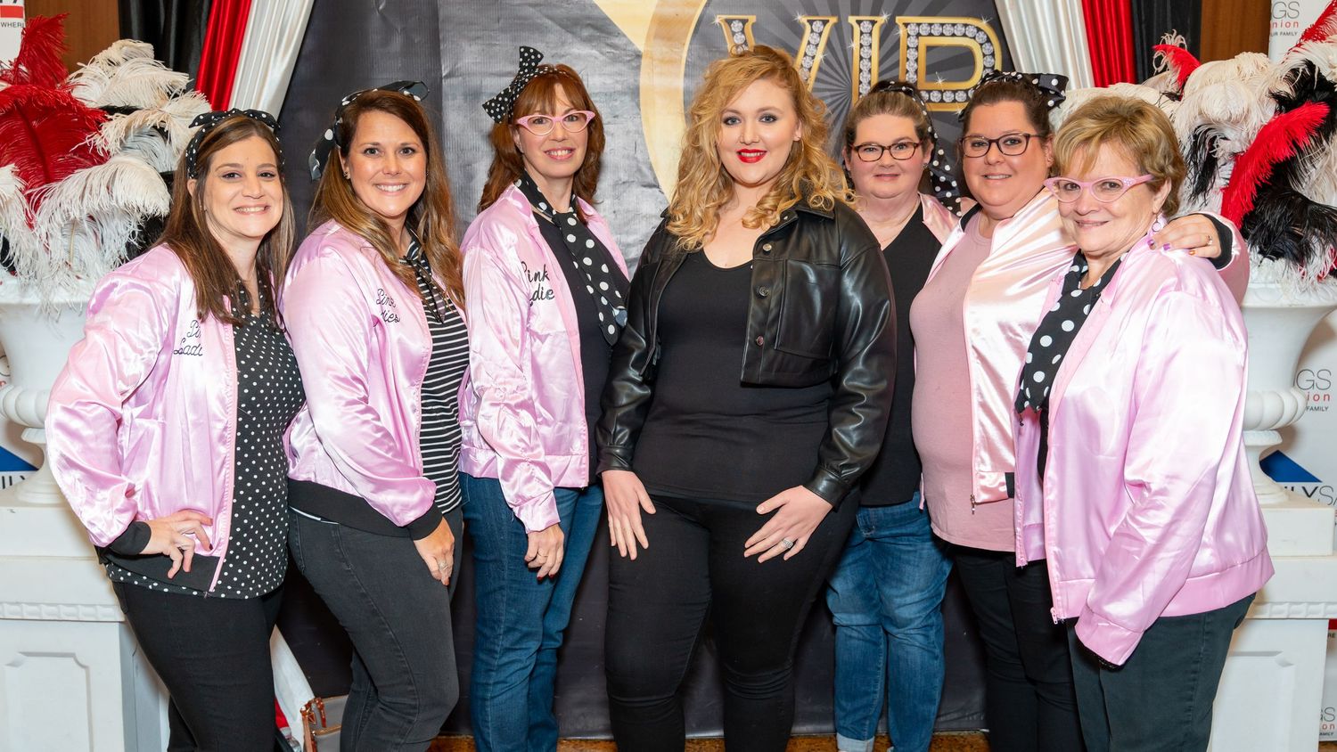 Group photo of people wearing pink jackets posing together at a formal event.