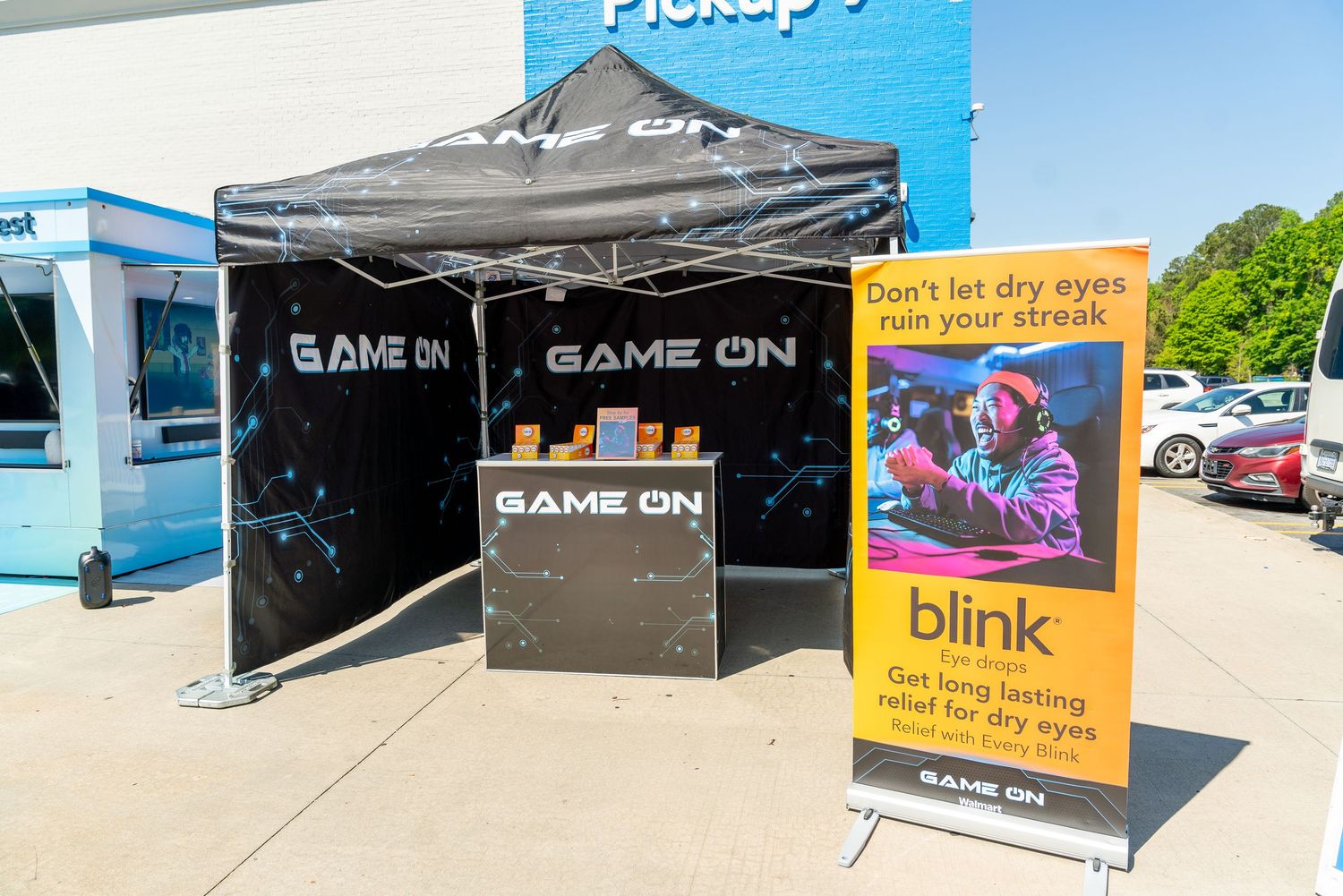 A black popup tent booth with 'Game On' branding and a promotional banner display stands outside a retail storefront.