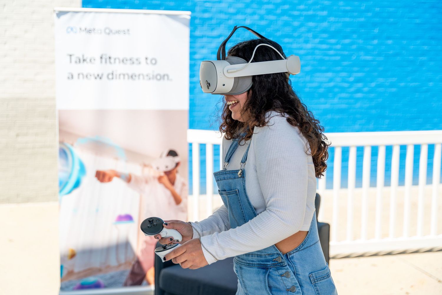 Someone wearing denim overalls and virtual reality headset plays interactive game against bright blue backdrop.