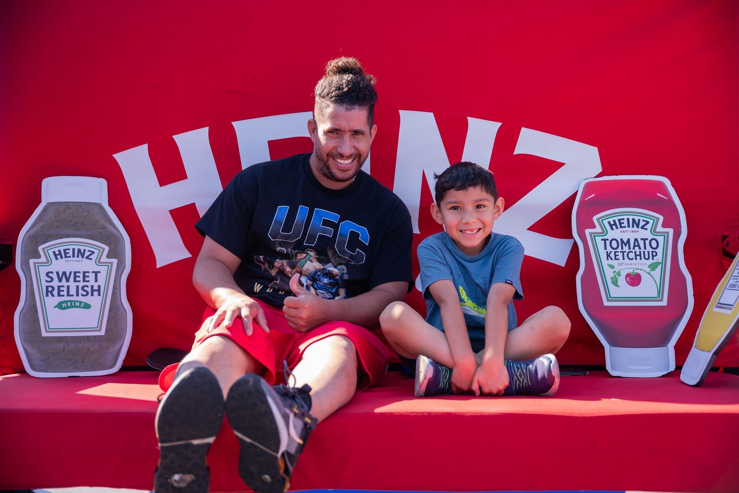 Father and son sitting on red bench with Heinz ketchup bottle decorations.