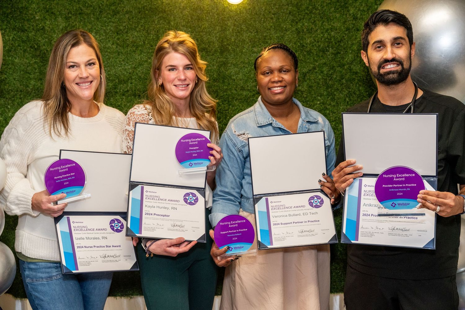 A group of happy award recipients pose together while holding up their purple and blue certificates.